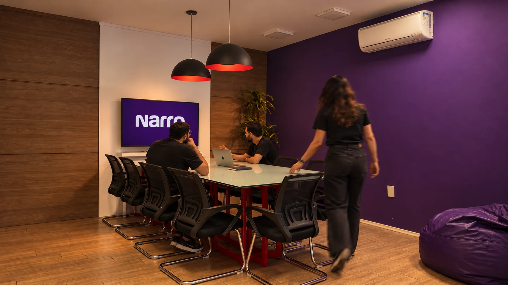 Sala de reunião da Narro em Campinas, com a parede roxa e a marca Narro na tela
